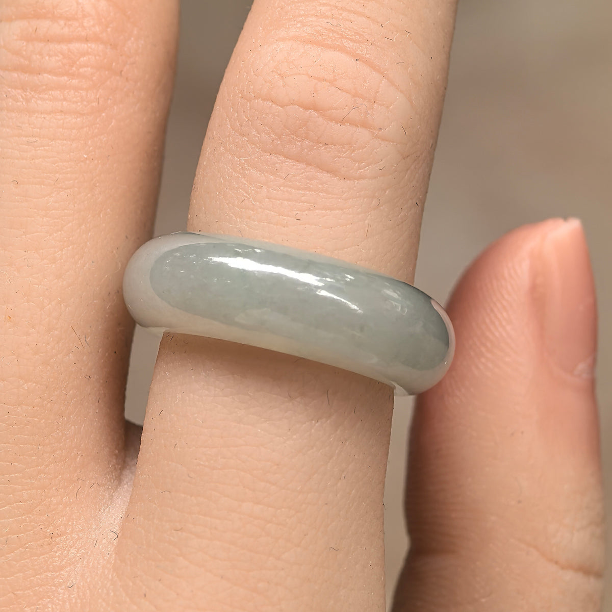 Front view of an icy glutinous pale green jadeite ring band on a finger, with light reflecting across its rounded outer surface.