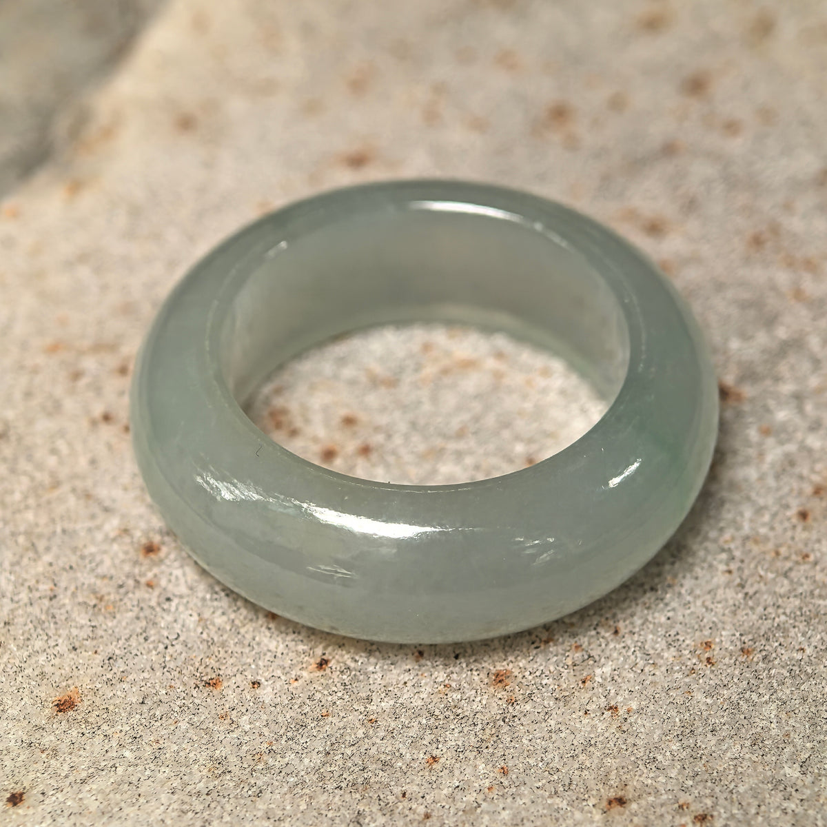 Angled view of a pale green jadeite ring band resting on stone, showing its substantial thickness and inner opening.