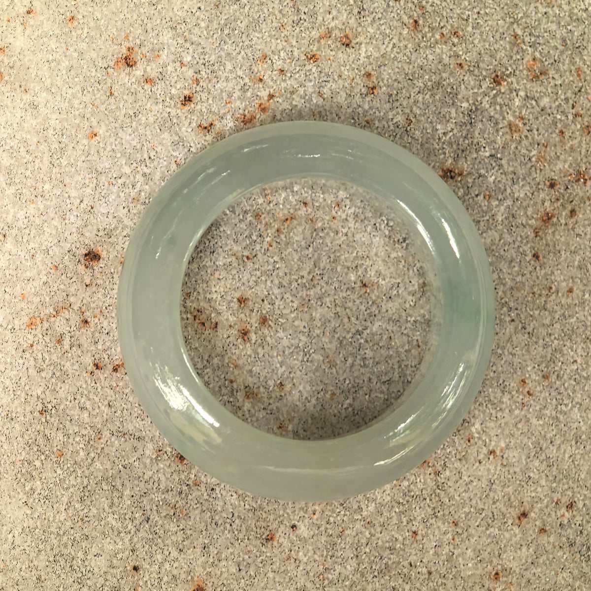 Overhead view of a pale green jadeite ring band on stone, showing its circular shape and softly translucent texture.
