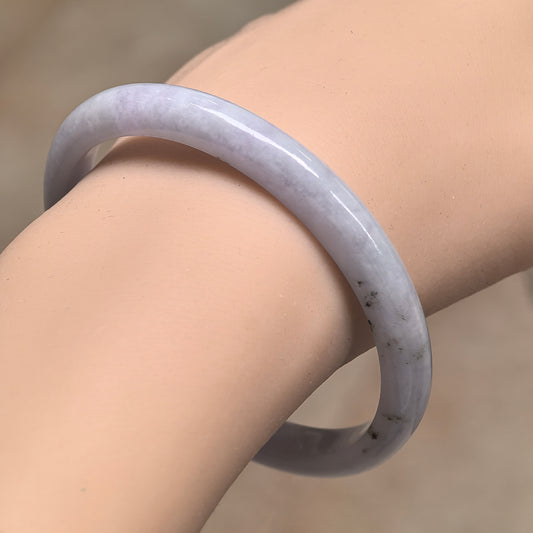 Angled wrist view of a slim white jadeite D-shape bangle with a polished surface and a cluster of black inclusions.