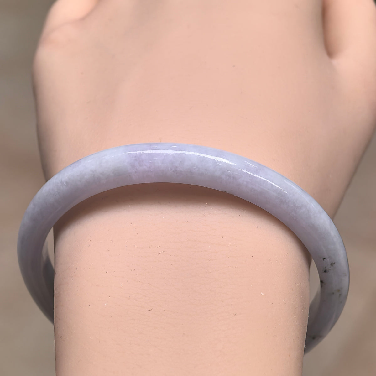 Front wrist view of a white glutinous jadeite bangle showing its narrow band, clouded texture and black inclusions along one side.