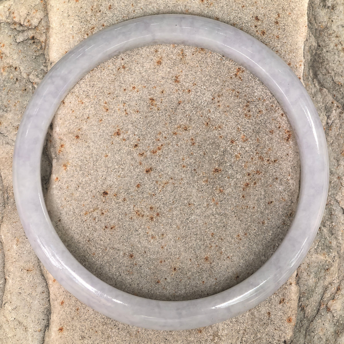 Overhead view of a slim white jadeite bangle on stone, showing its circular outline and softly clouded texture.