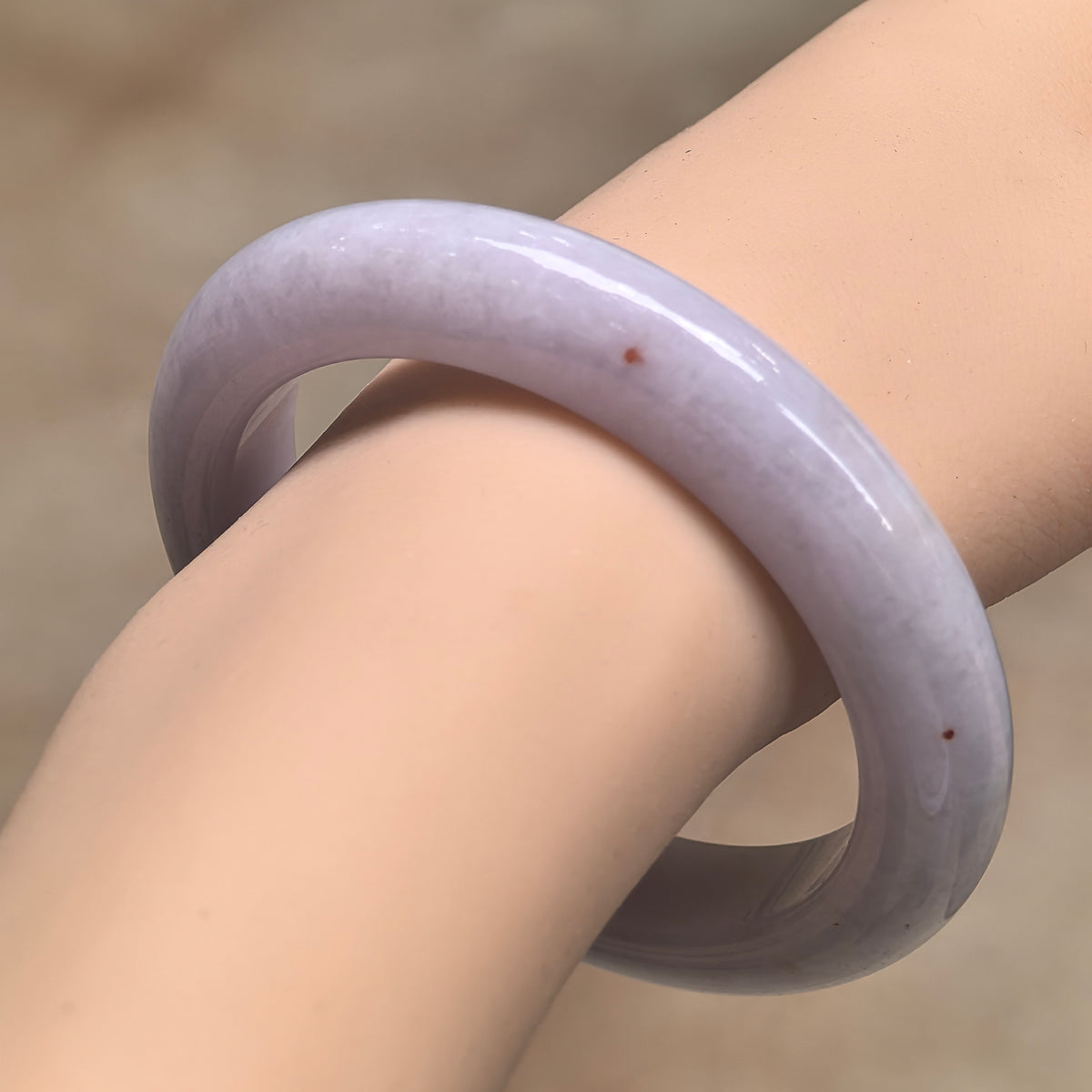 Angled wrist view of a pale lavender jadeite D-shape bangle with small golden-brown flecks and a polished outer surface.