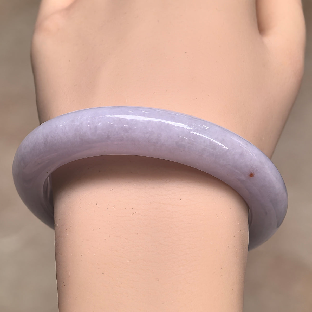 Front wrist view of a glutinous pale lavender jadeite bangle, showing its softly clouded texture and a localized golden-brown fleck.