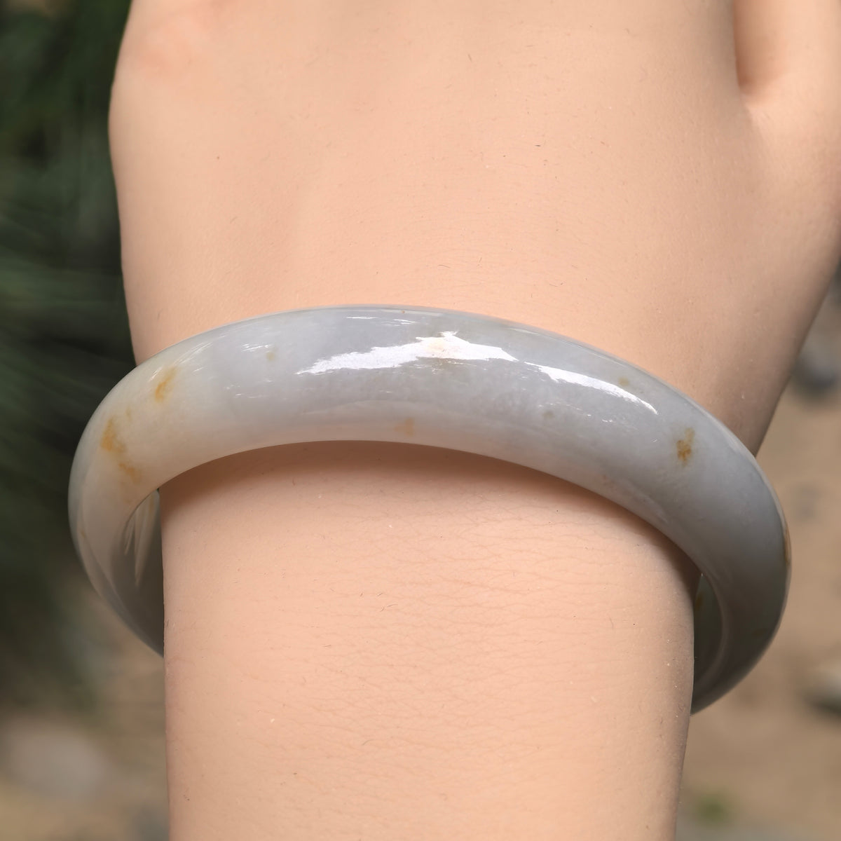 Front wrist view of a fine glutinous jadeite bangle, showing its broad white and pale green band with natural golden-brown markings.