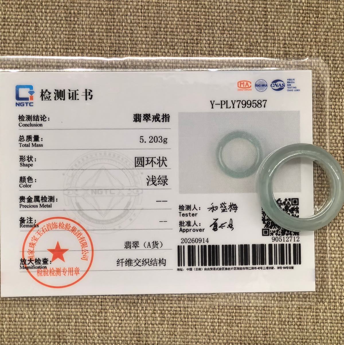Pale green jadeite ring band displayed with its matching NGTC certificate on woven fabric.