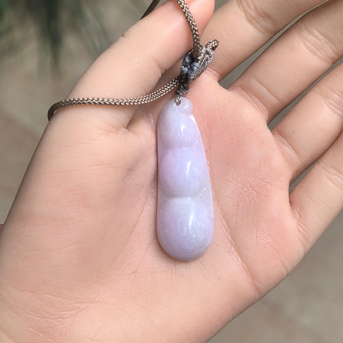 Glutinous pale lavender jadeite Bean Pod Pendant resting in a palm, showing its elongated proportions and decorative cord knot.