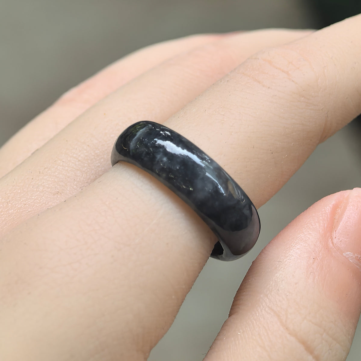 Angled view of a gray-black jadeite ring band worn on a finger, showing smoky mottling and a glossy rounded outer surface.