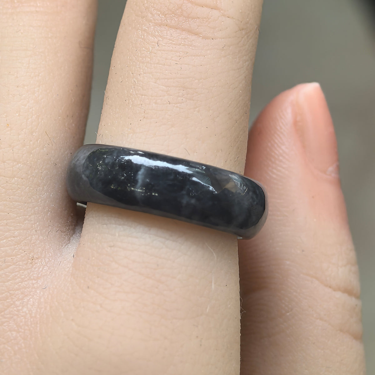 Front view of a glutinous gray-black jadeite ring band on a finger, showing deep black areas and softer gray patches.