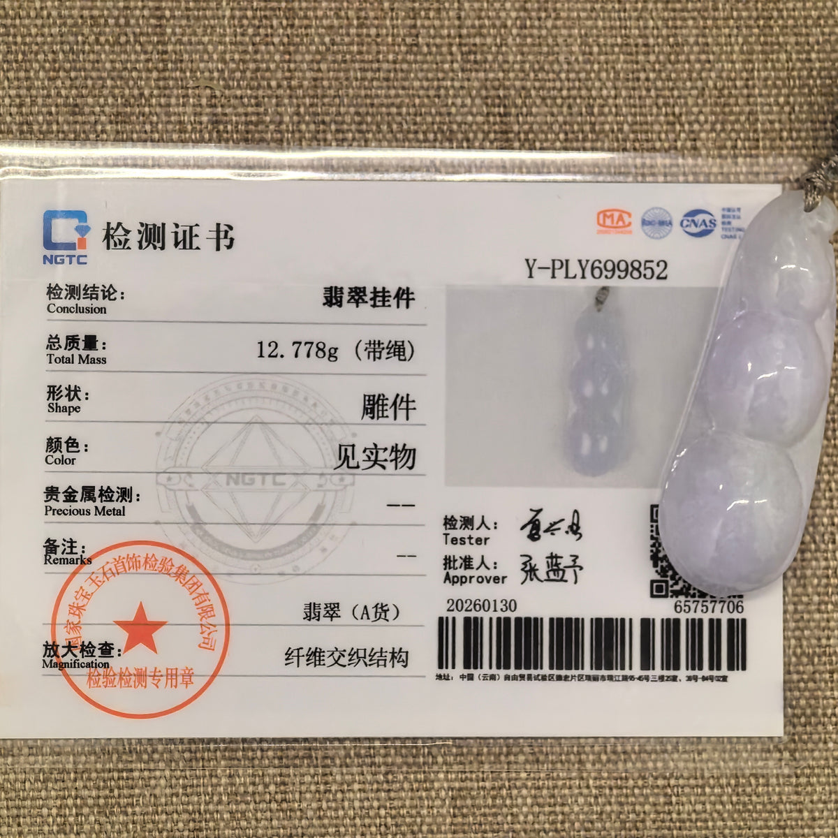 Pale lavender jadeite Bean Pod Pendant displayed with its matching NGTC certificate on woven fabric.