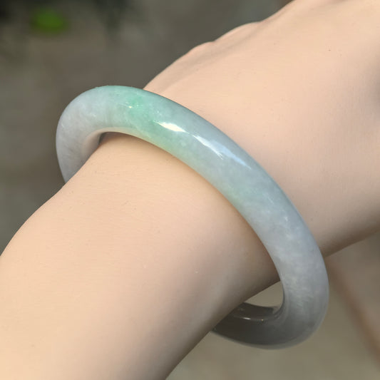 Angled wrist view of a glutinous jadeite round-bar bangle, showing pale lavender and pale green sections along the rounded profile.