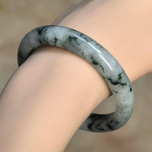 Angled wrist view of a glutinous D-shape jadeite bangle with deep green floating patterns across a pale green base.