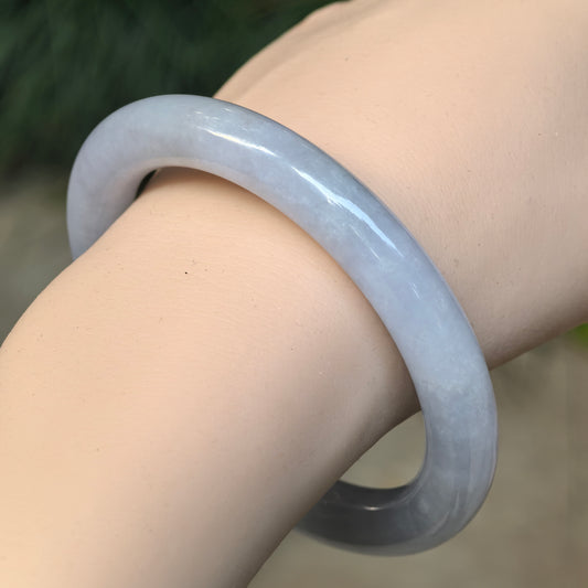 Angled wrist view of a very pale lavender round-bar jadeite bangle with a faint blue-lavender tone and a polished finish.