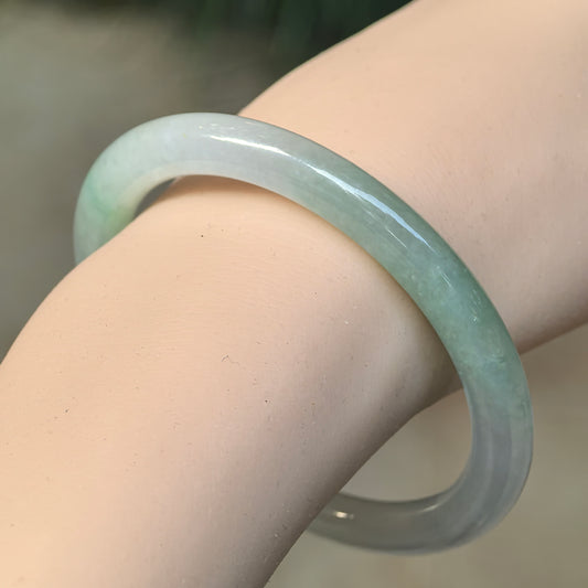 Angled wrist view of an icy glutinous light green round-bar jadeite bangle showing its slender profile and polished luster.
