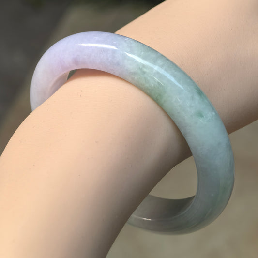 Angled wrist view of a glutinous jadeite D-shape bangle, showing the transition from pale lavender to pale green.