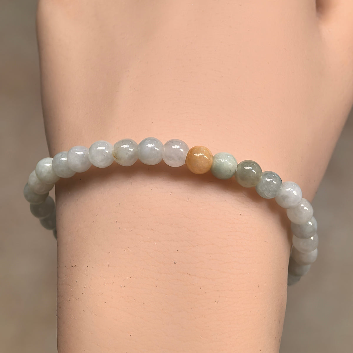 Front wrist view of the pale green jadeite bead bracelet, showing polished round beads and a yellow accent.