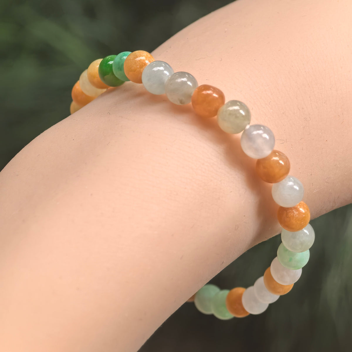 Angled wrist view of a multicolor jadeite bead bracelet, showing polished green, white and orange-brown round beads.