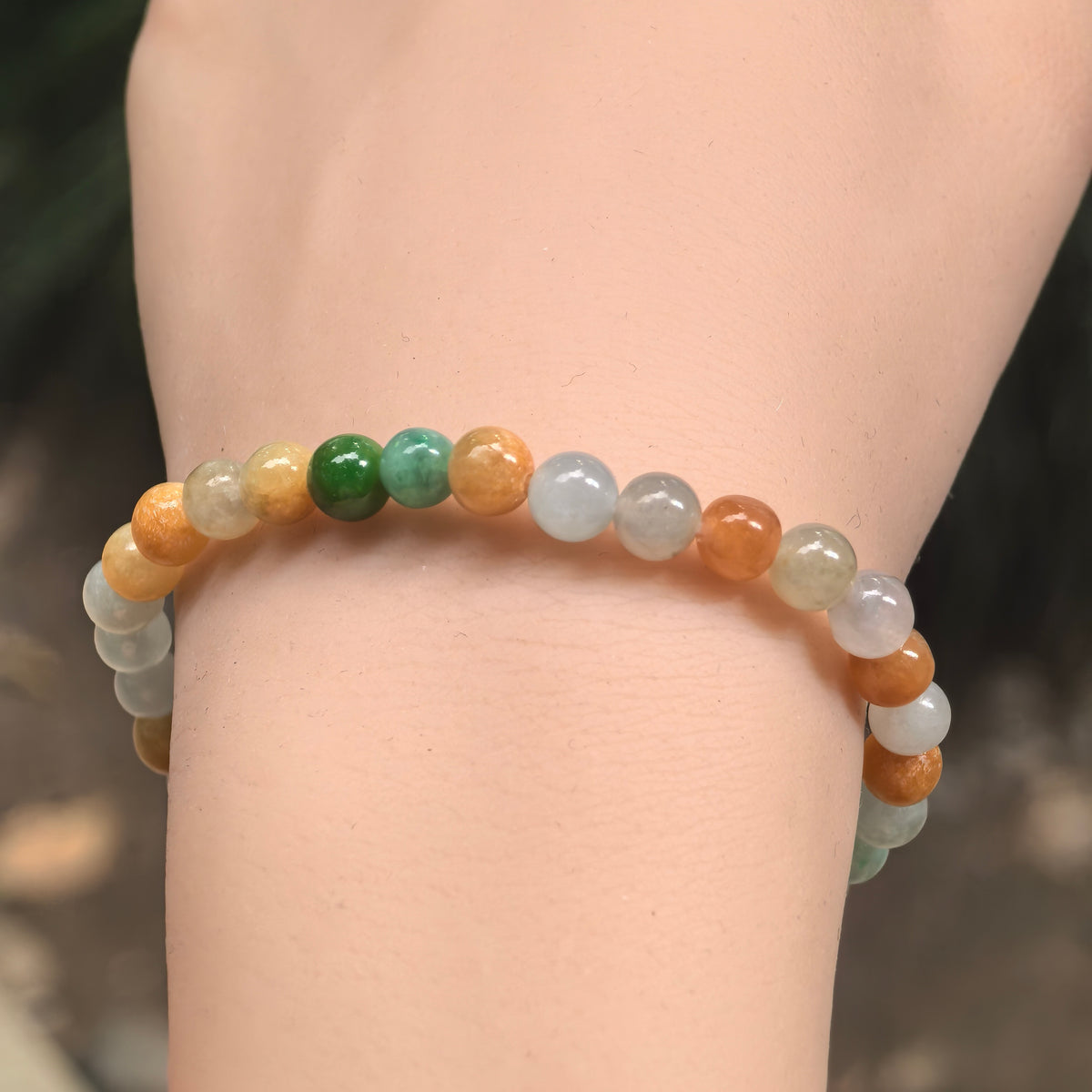 Front wrist view of a glutinous multicolor jadeite bracelet, showing the arrangement of green, white, yellow and orange-brown beads.
