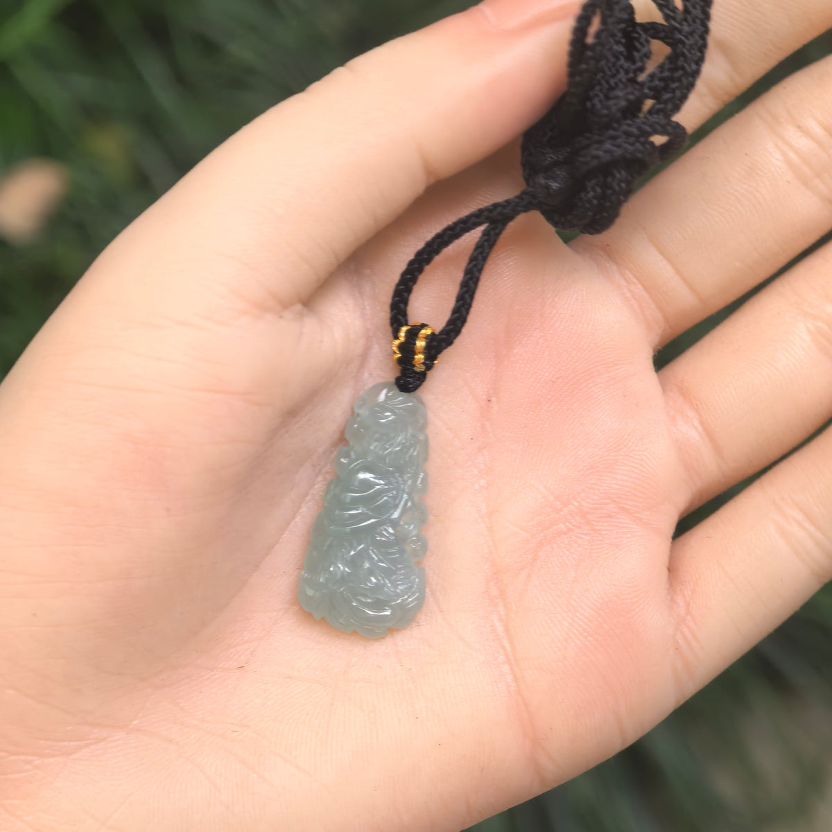 Icy glutinous light blue jadeite phoenix pendant resting in a palm, with its black braided cord and decorative knot visible.