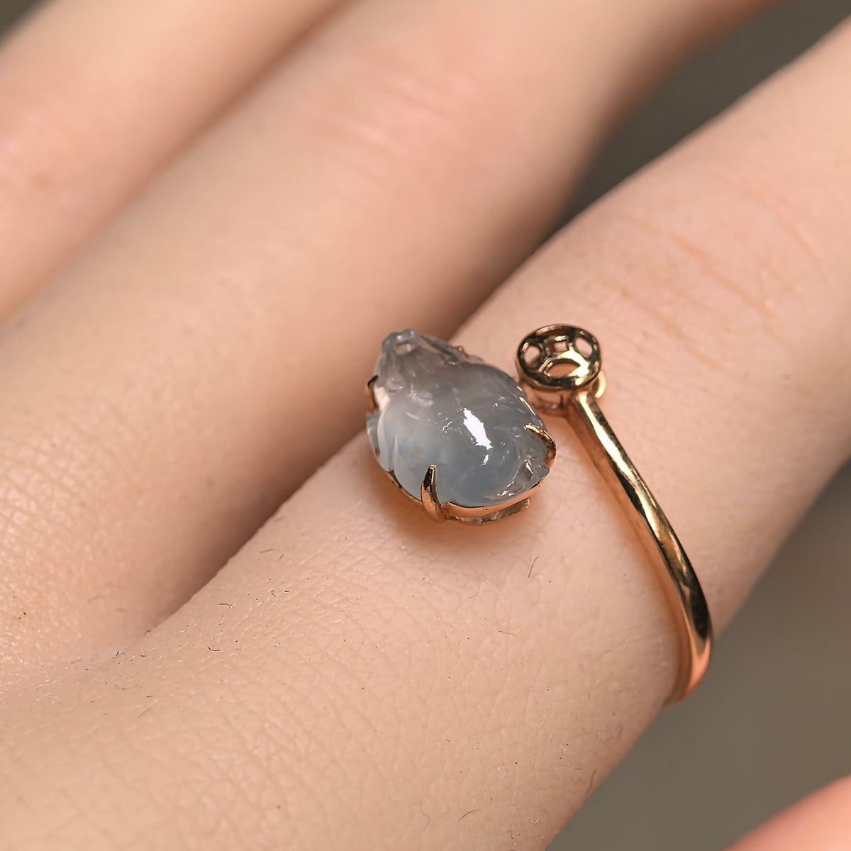 Angled view of an icy white jadeite Pixiu ring worn on a finger, showing its 18K gold setting and open band.