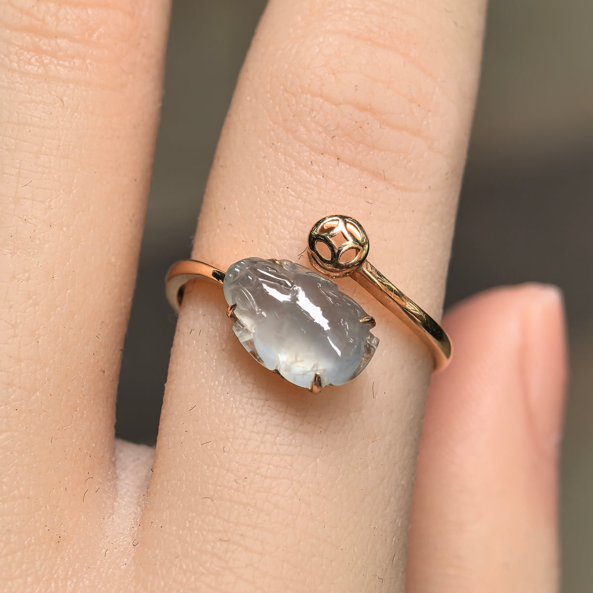 Front view of the white jadeite Pixiu ring on a finger, with a carved Pixiu beside an openwork gold coin motif.