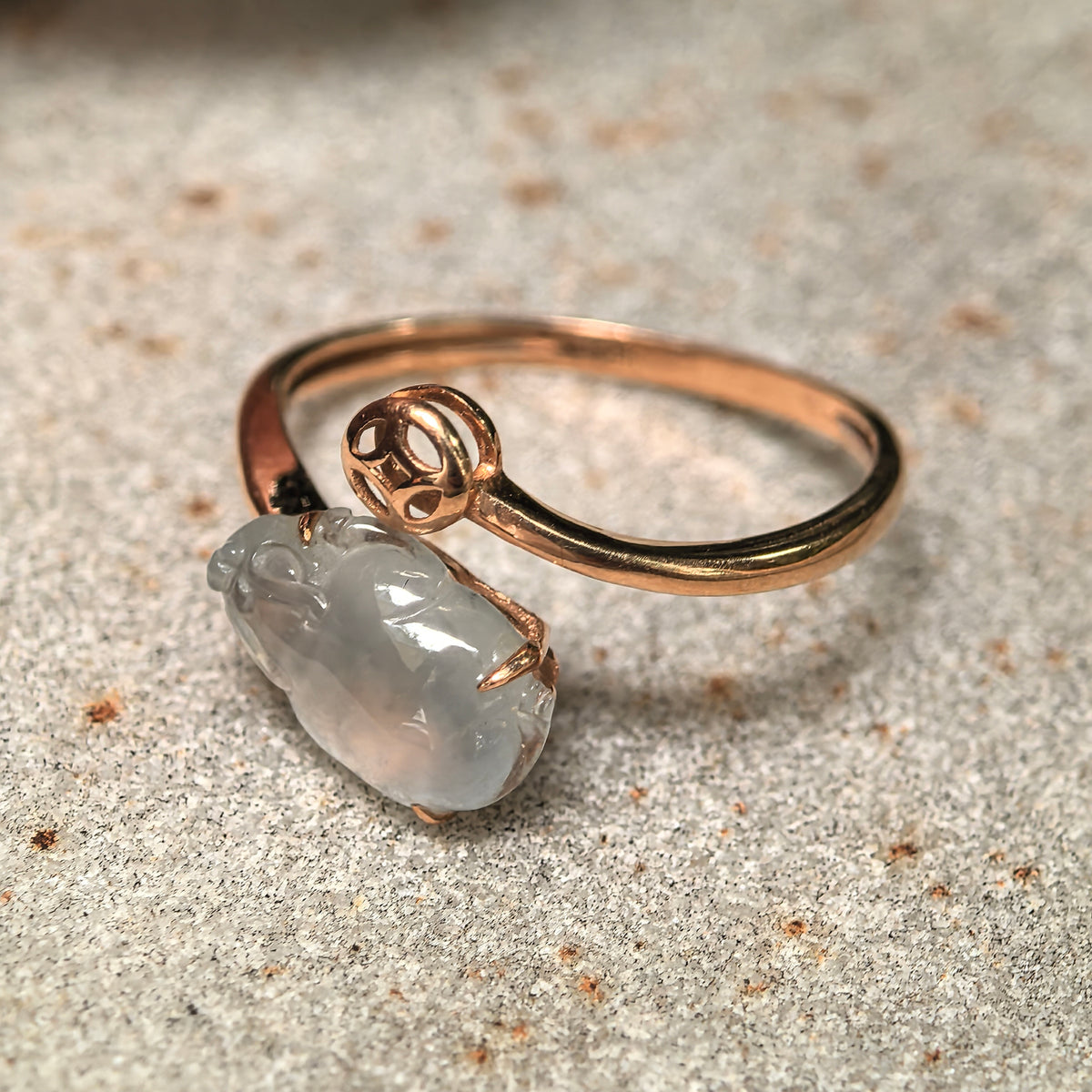 Angled view of the white jadeite Pixiu ring resting on stone, showing the slim gold band and coin motif.