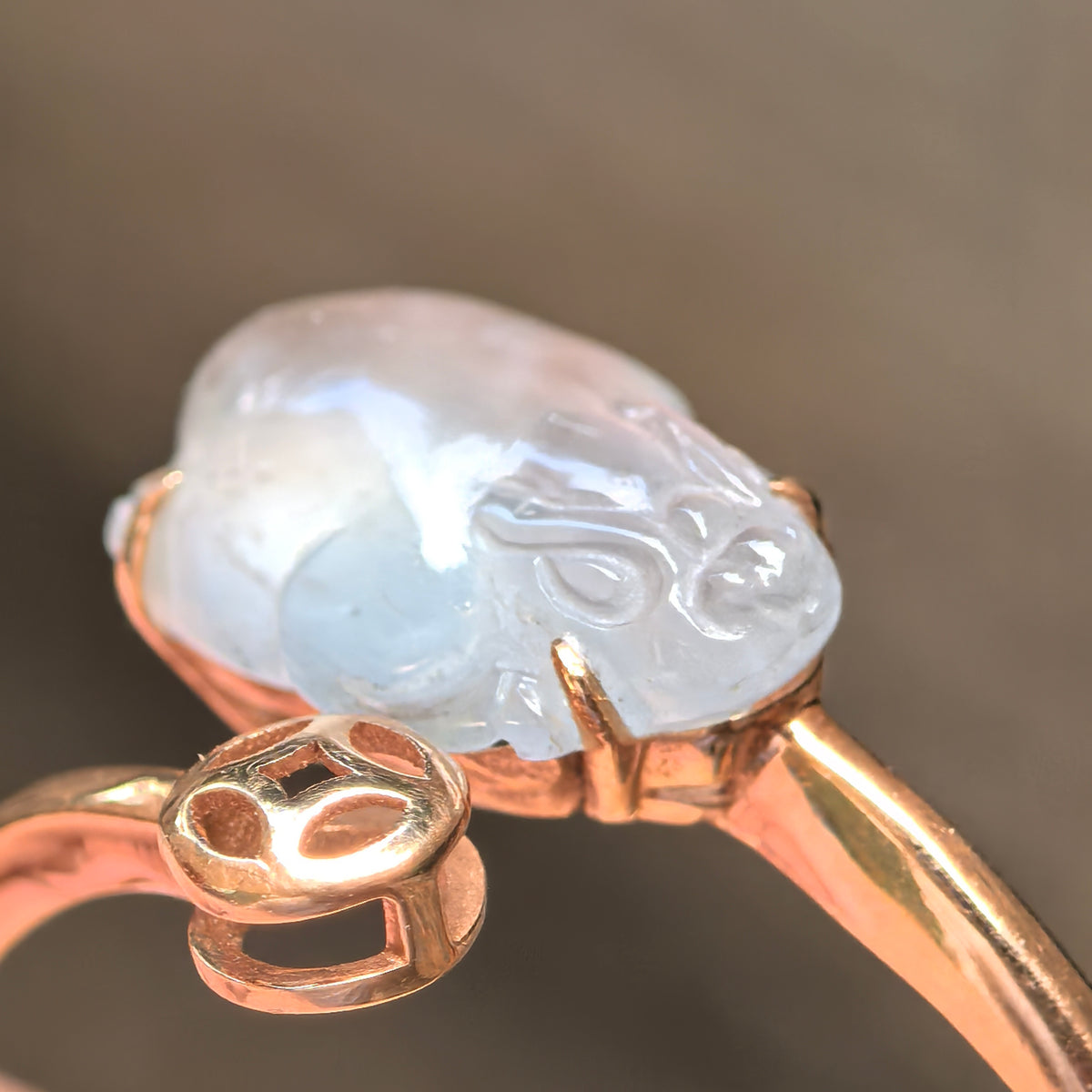 Macro view of the icy white jadeite Pixiu carving, showing its face, 18K gold prongs and openwork coin detail.