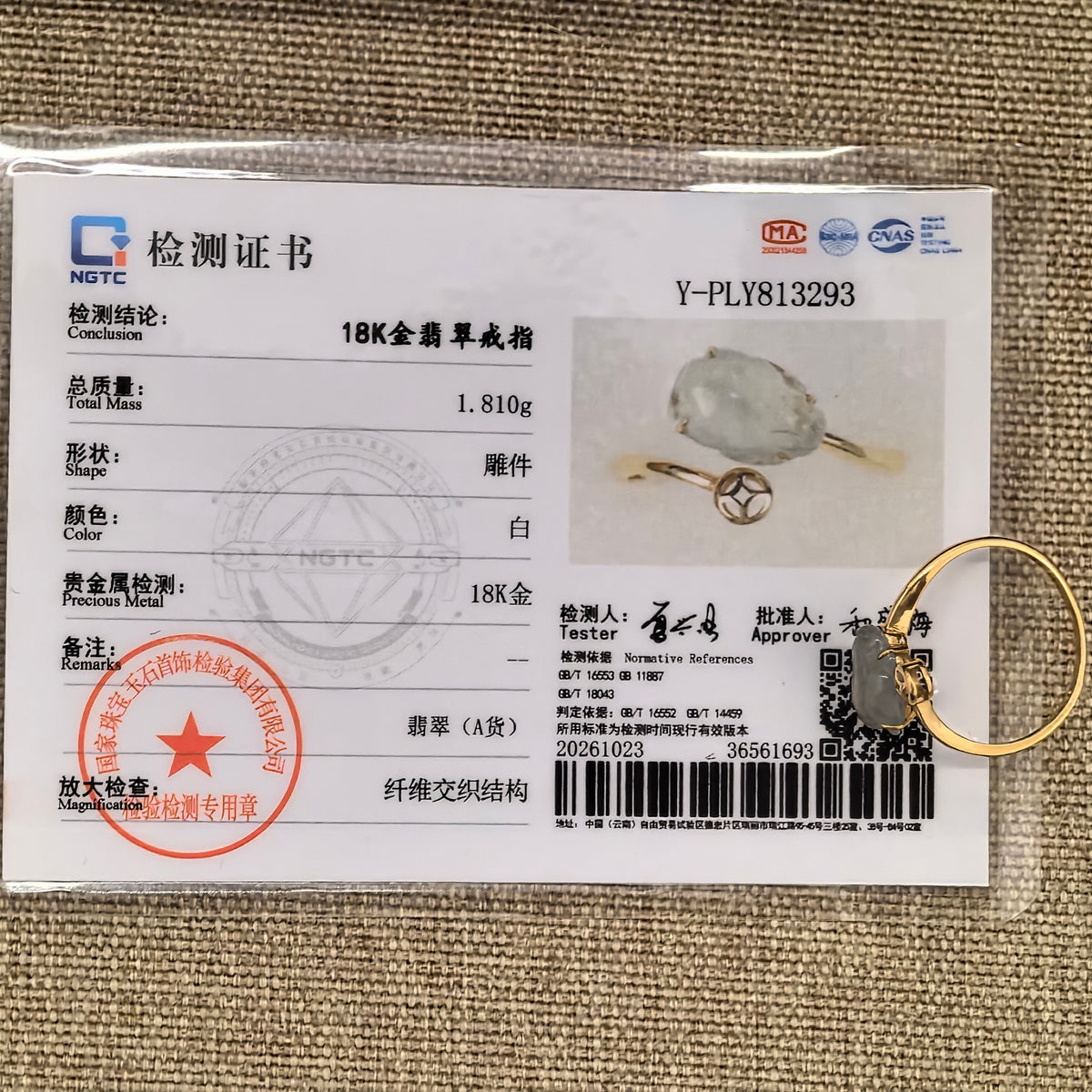 White jadeite Pixiu ring in 18K gold beside its matching NGTC certificate on tan woven fabric.