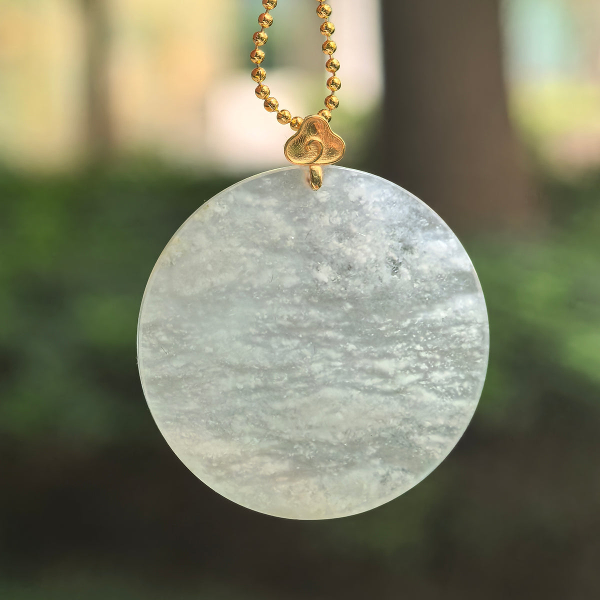 White jadeite Plain Plaque Pendant hanging from a chain, with flowing snowflake inclusions, a pale green undertone and an 18K gold bail with a cloud motif.
