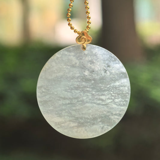 White jadeite Plain Plaque Pendant hanging from a chain, with flowing snowflake inclusions, a pale green undertone and an 18K gold bail with a cloud motif.