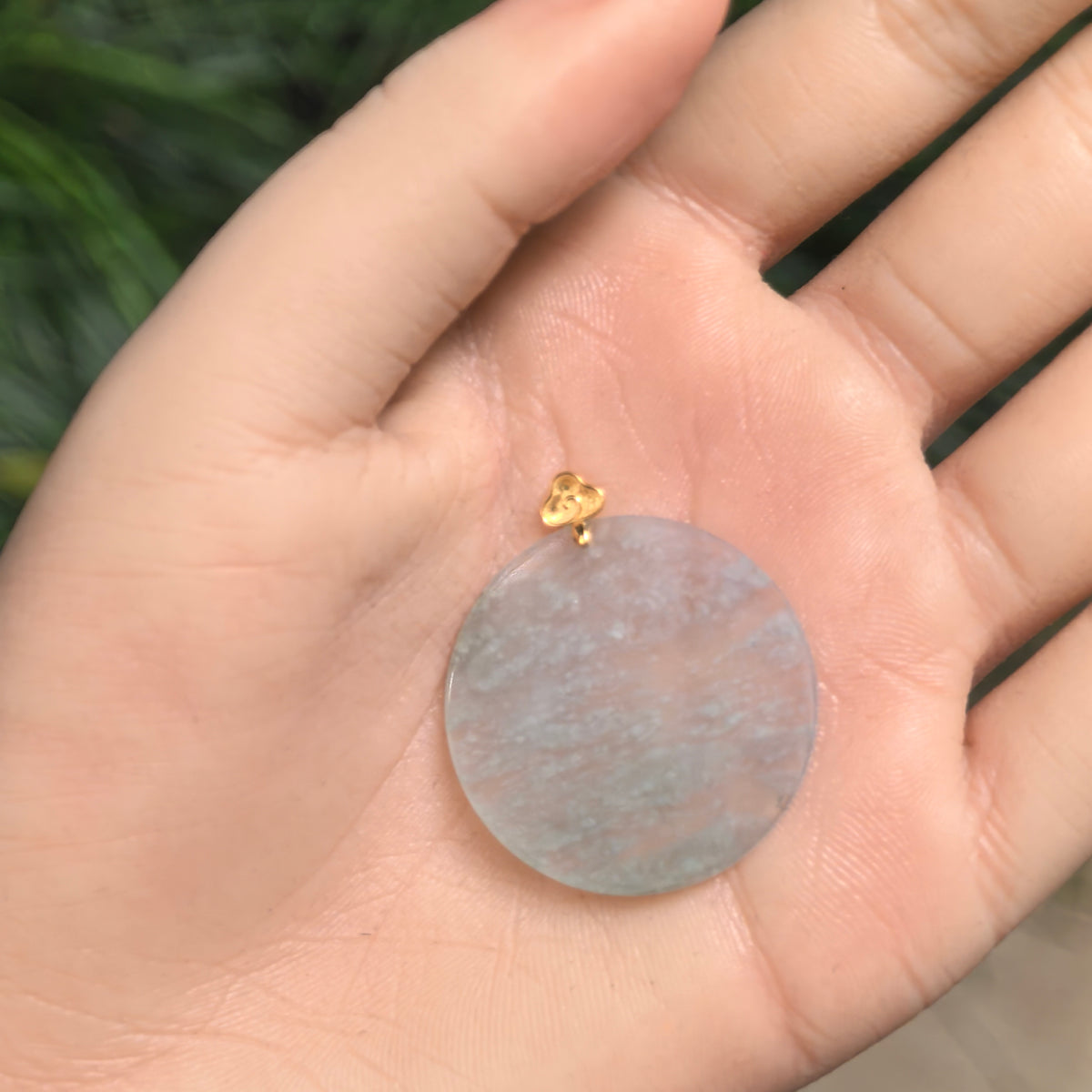 Round icy white jadeite Plain Plaque Pendant resting in an open palm, showing its translucent face, snowflake-like inclusions and small 18K gold bail.
