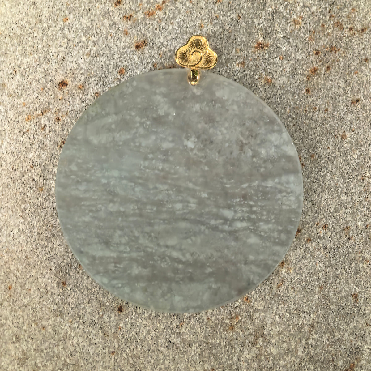 Front view of the round white jadeite Plain Plaque Pendant on stone, showing bands of snowflake-like inclusions and the curling cloud detail on its gold bail.