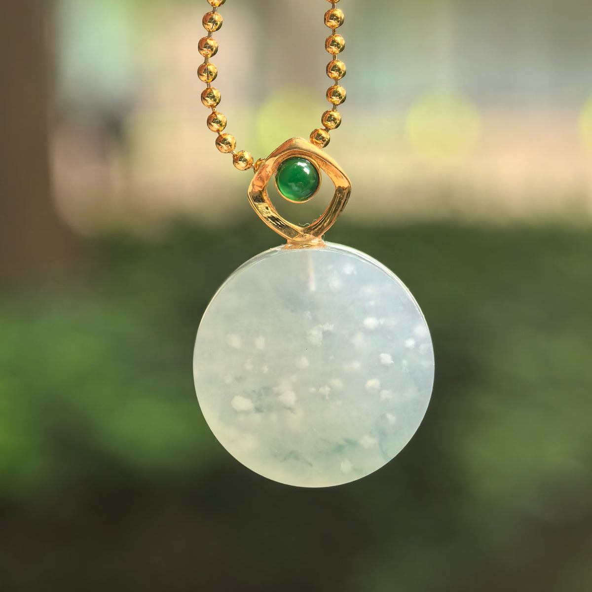 Icy white jadeite Plain Plaque Pendant hanging from a chain, showing snowflake-like inclusions, a pale green undertone and an 18K gold bail with a green accent stone.