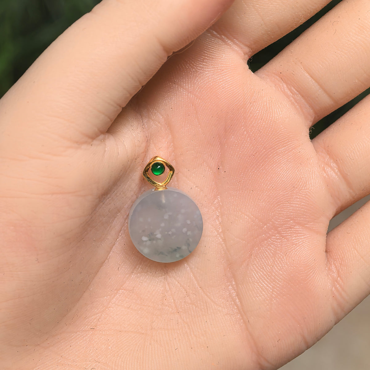 Round white jadeite Plain Plaque Pendant resting in an open palm, showing its natural snowflake pattern and geometric gold bail.