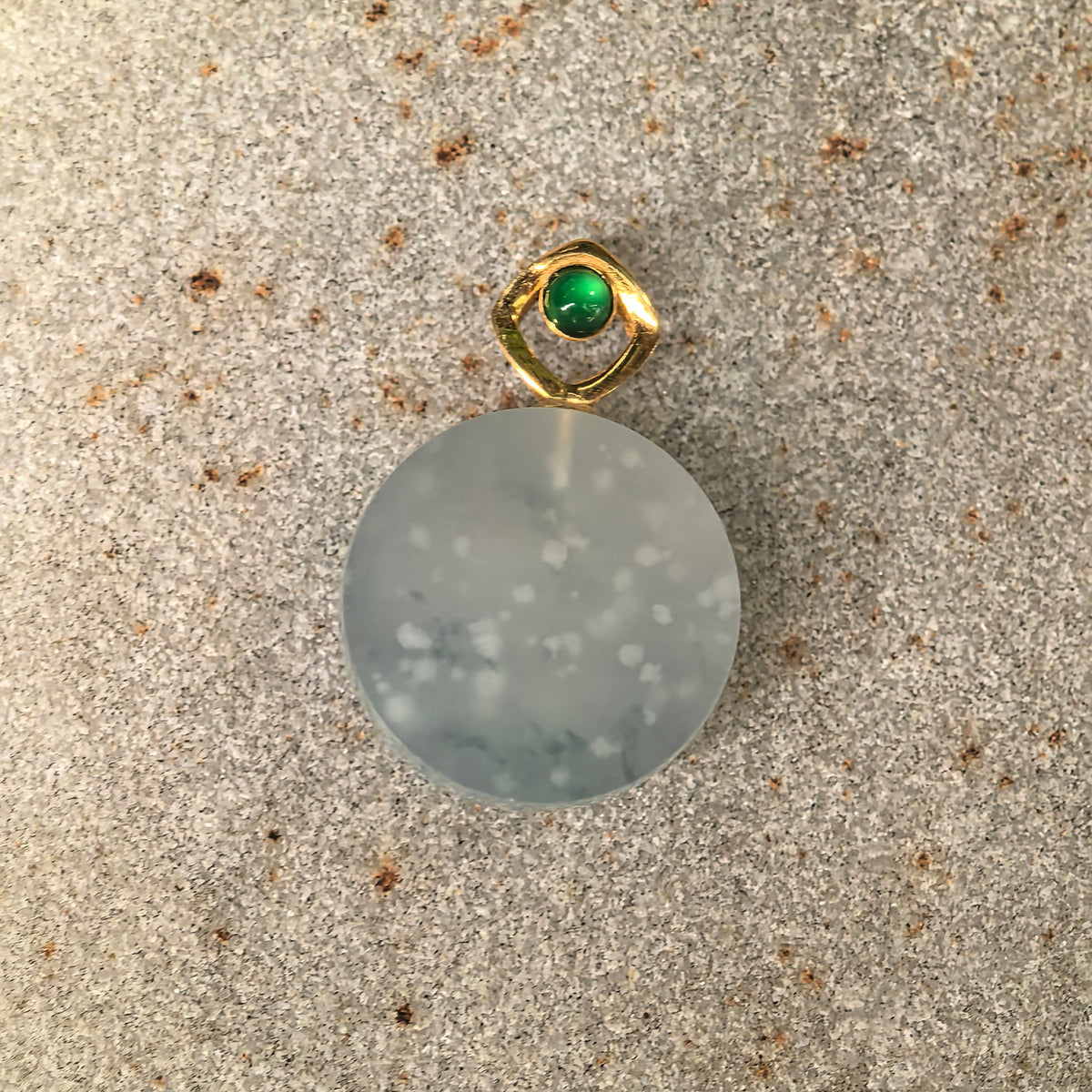 Front view of the icy white jadeite Plain Plaque Pendant on stone, showing snowflake-like inclusions across the circular face and its 18K gold bail.