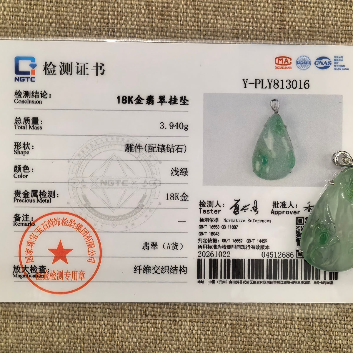 Light green jadeite butterfly and lotus pendant in 18K gold with diamonds beside its matching NGTC certificate on woven fabric.