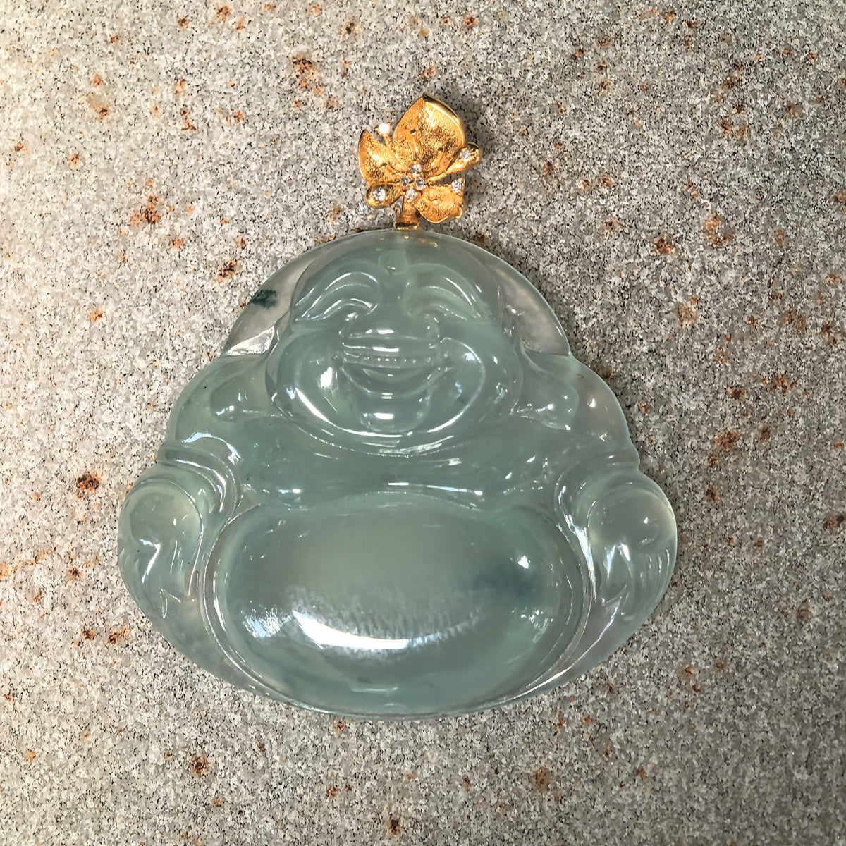 Close-up front view of a light green jadeite Laughing Buddha pendant with detailed robes, deeper green accents and an 18K gold botanical bail.