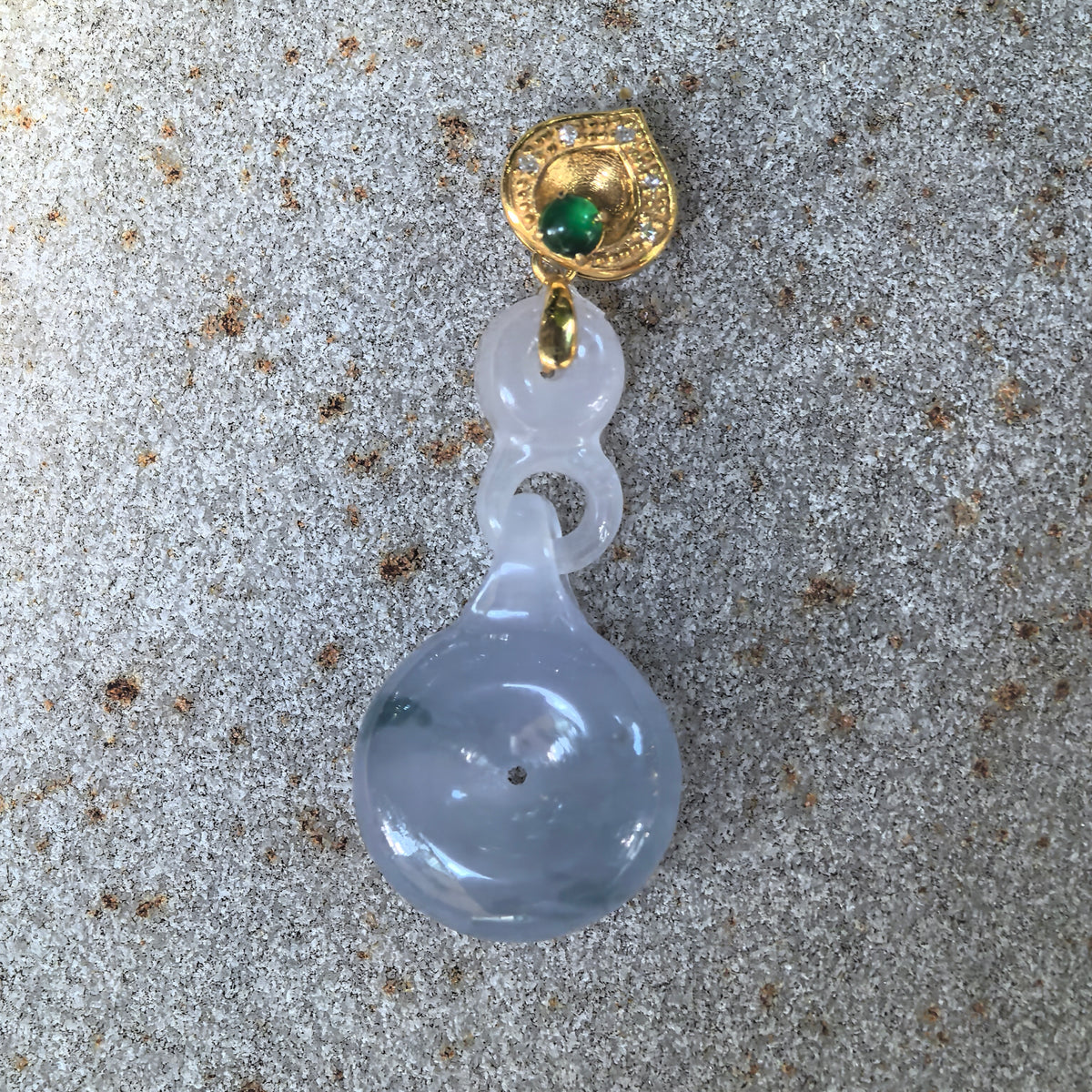 Front view of the purple jadeite Peace Pendant on stone, showing green patches, carved jadeite links, and a gold bail edged with diamonds and accented with a green stone.
