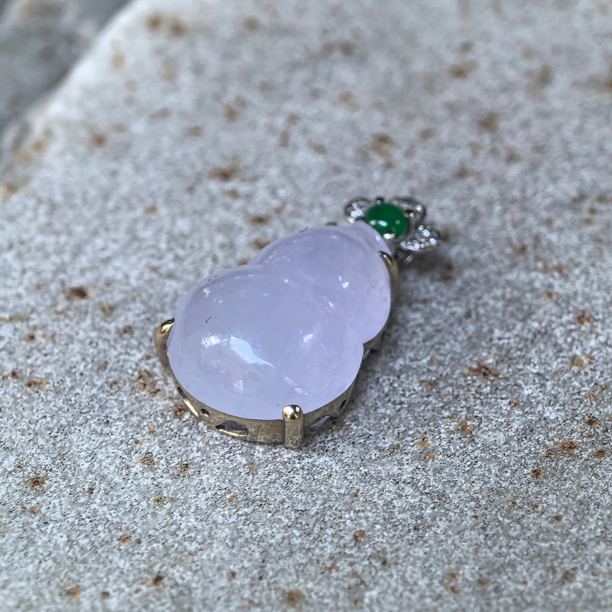 Angled view of the purple jadeite Gourd Pendant on stone, showing its domed profile, polished contours, and the side details of the gold setting.