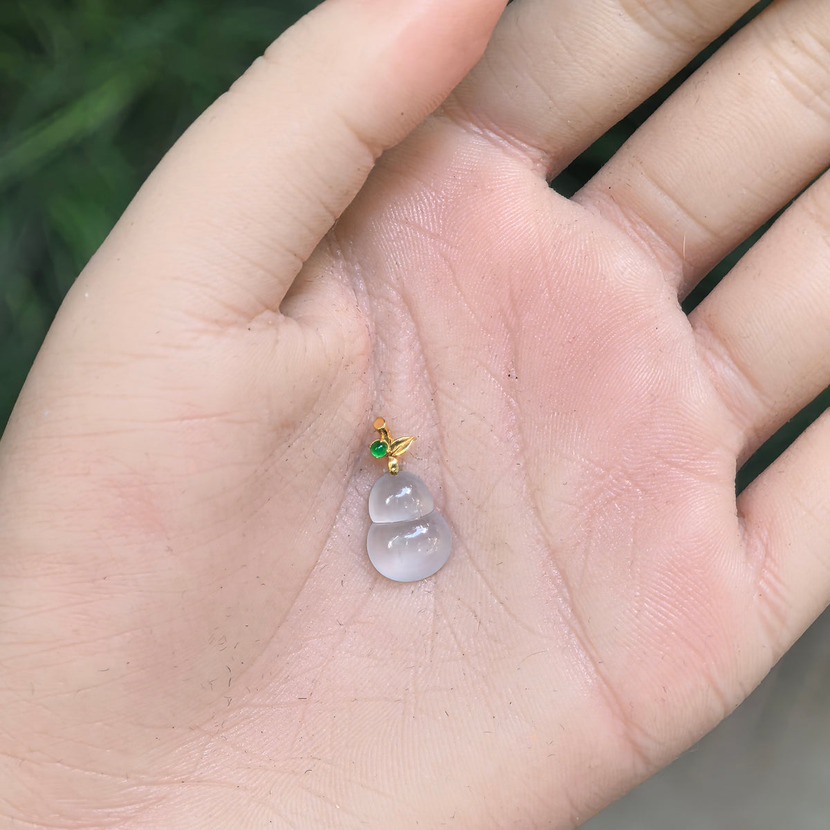White jadeite Gourd Pendant resting in an open palm, showing its compact proportions, rounded lobes, and decorative gold bail.