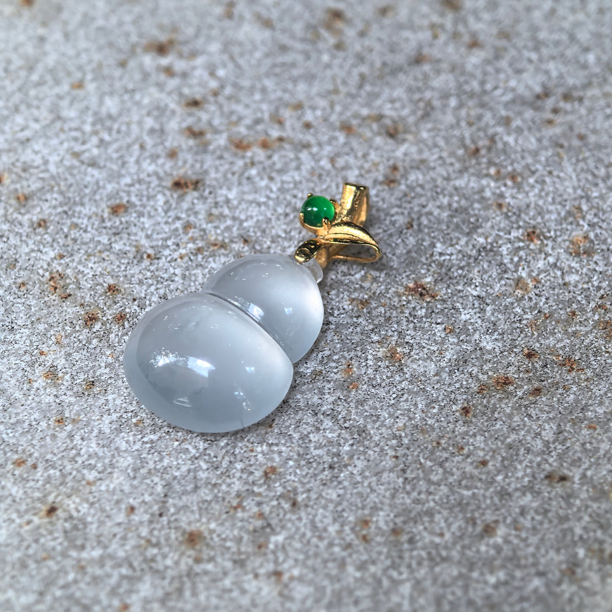Angled view of the white jadeite Gourd Pendant on stone, showing its domed contours, narrow waist, and green accent stone in the gold bail.