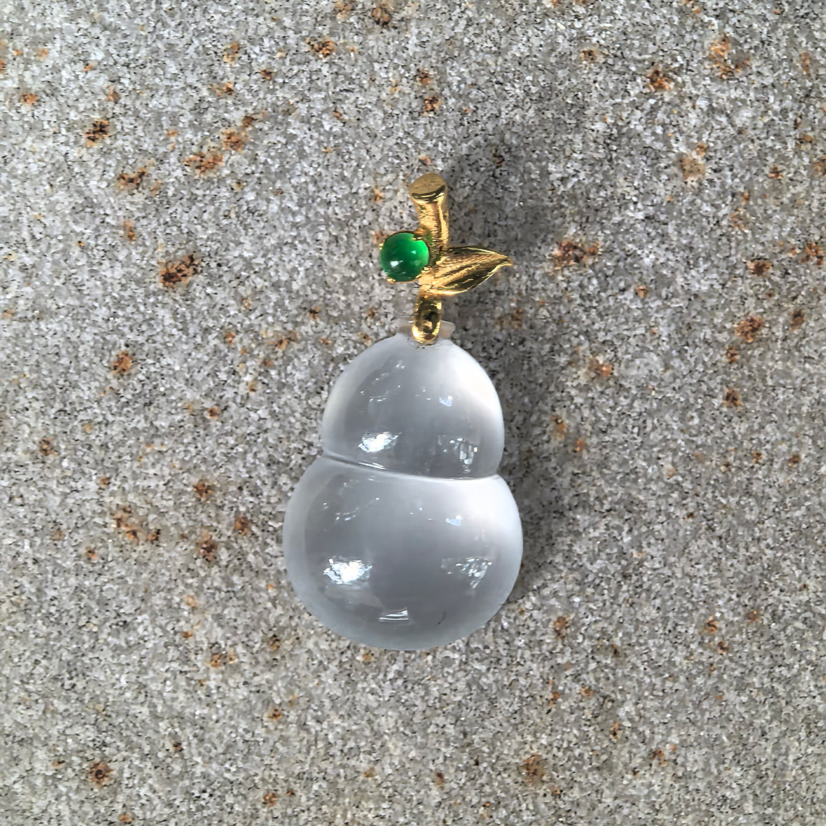 Front close-up of the white jadeite Gourd Pendant on stone, showing its translucent body, crisp surface reflections, and 18K gold stem and leaf details.