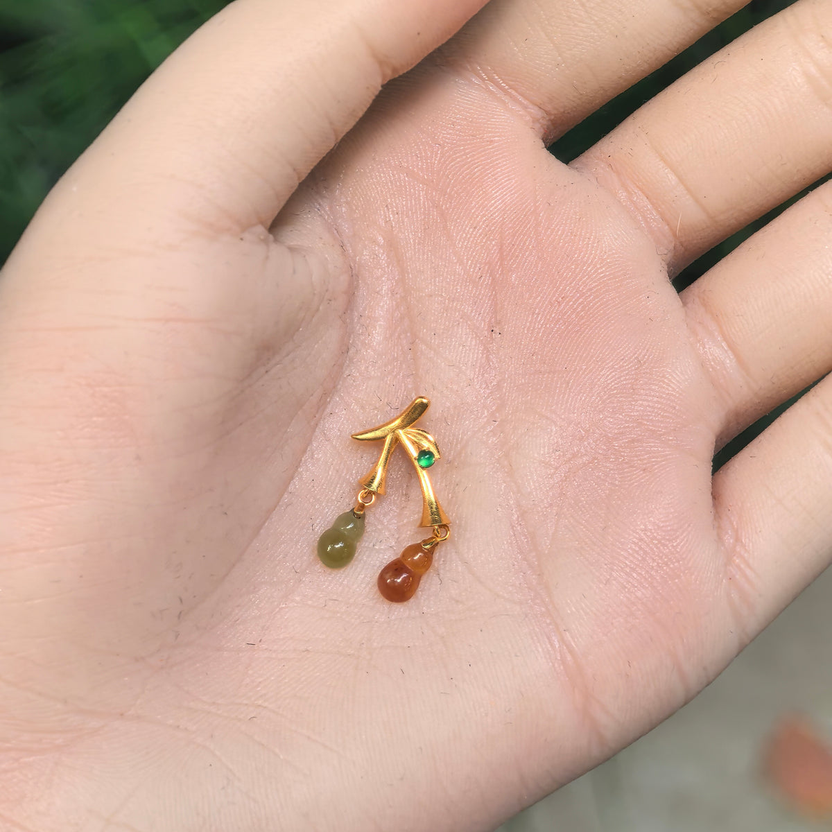 Petite red and yellow jadeite double Gourd Pendant resting in an open palm, showing its miniature scale and asymmetric 18K gold design.