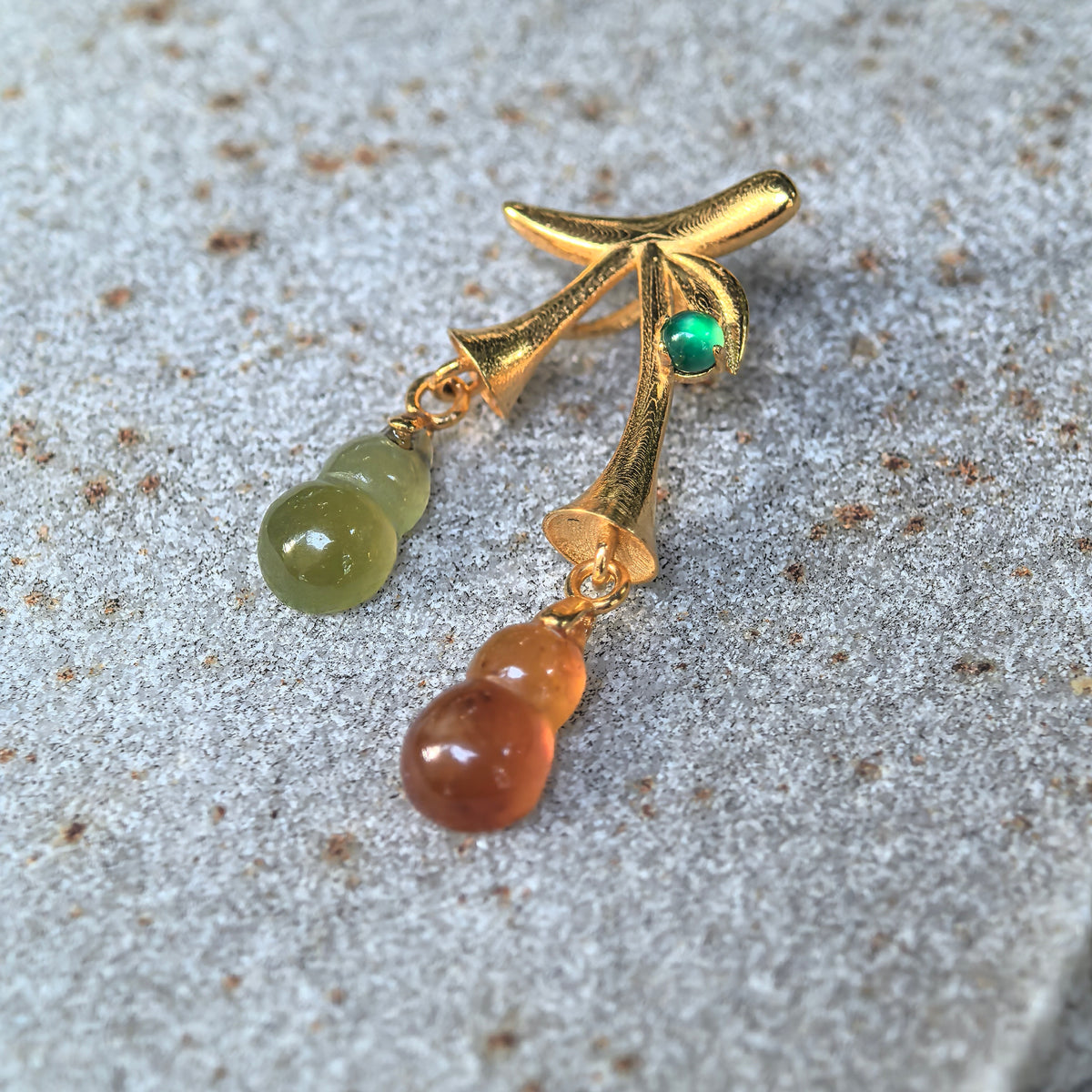 Angled close-up of the red and yellow jadeite double Gourd Pendant on stone, showing polished carvings, connecting gold loops, and the leaf detail.