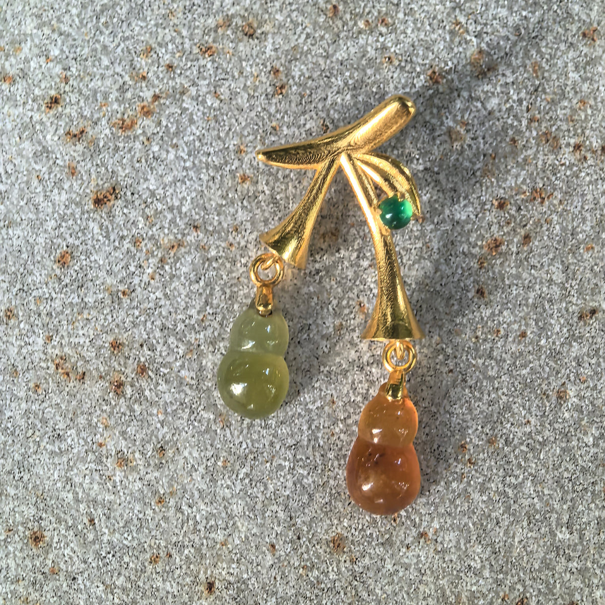 Front view of the red and yellow jadeite double Gourd Pendant on stone, showing the staggered drops, textured gold stems, and small green accent stone.