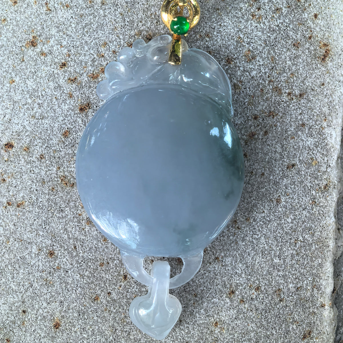 Front view of the purple jadeite Plain Plaque Pendant on stone, showing the carved upper crest, smooth round face, movable heart drop, and green accent stone in the gold bail.