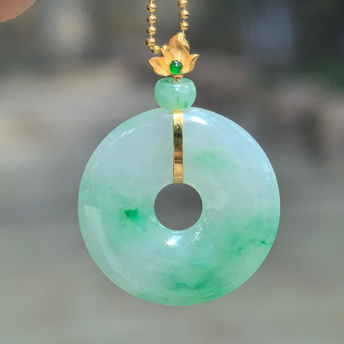 Icy glutinous light green jadeite Peace Pendant hanging from a chain, with floating green patterns, a green spacer bead, and an 18K gold floral bail.