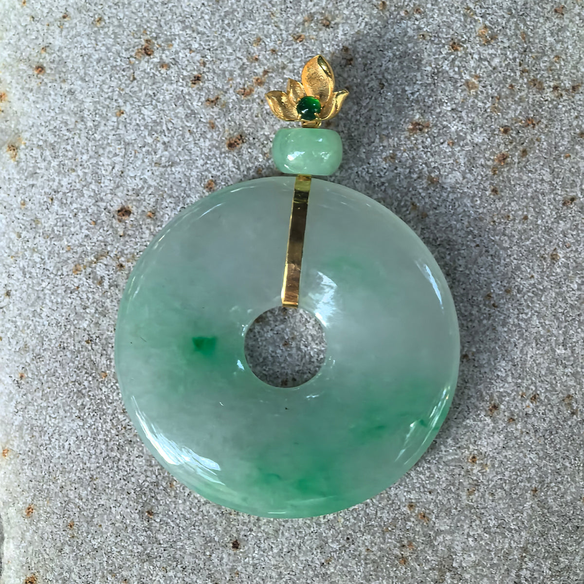 Front view of the light green jadeite Peace Pendant on stone, showing its round outline, central opening, and green patterns across the lower section.