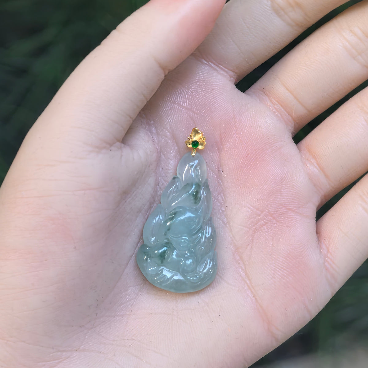 Light green jadeite Nine-Tailed Fox Pendant resting in an open palm, showing its elongated silhouette and the green accent stone in its floral gold bail.