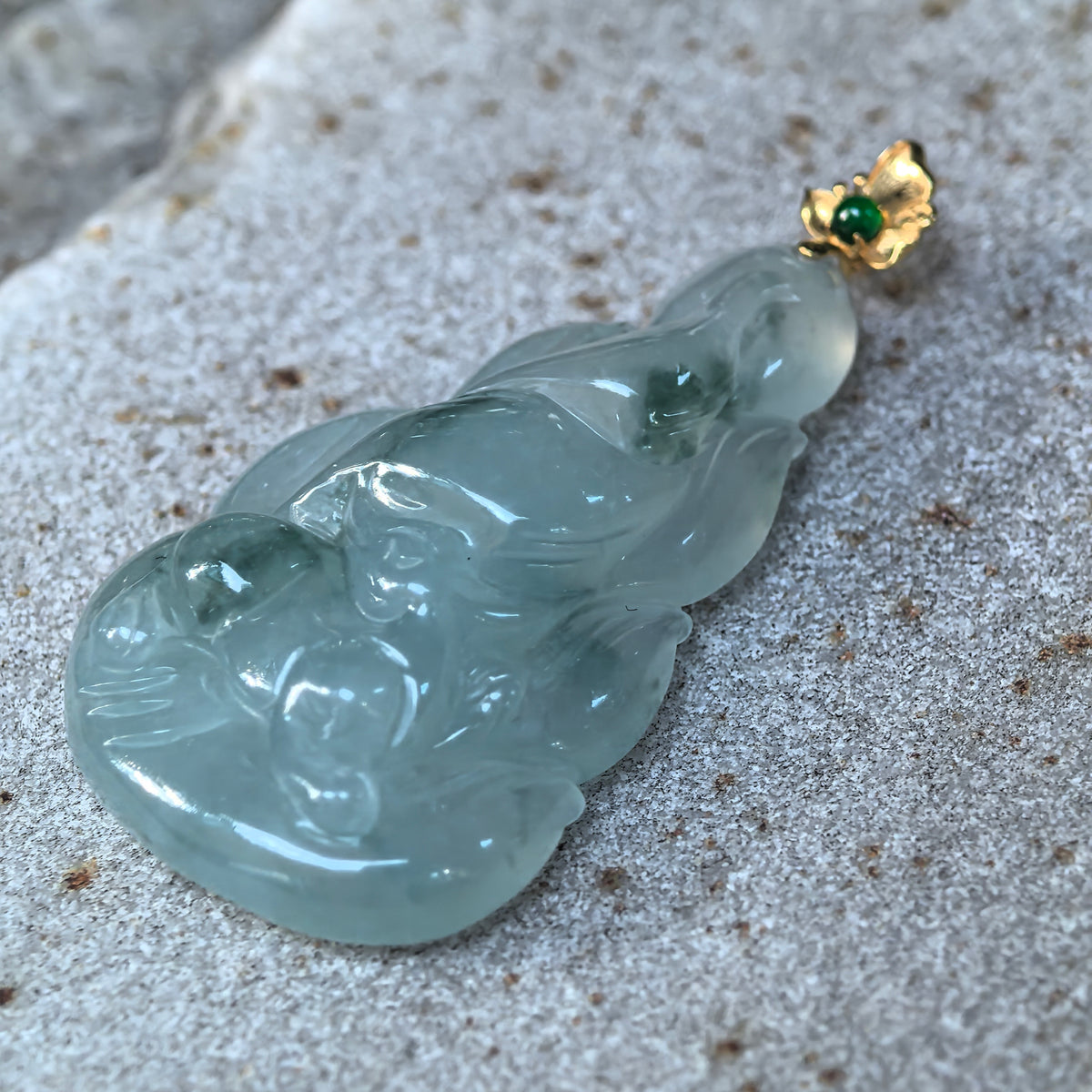 Angled close-up of the light green jadeite Nine-Tailed Fox Pendant on stone, showing the fox face, layered tail carving, and deeper green patches.